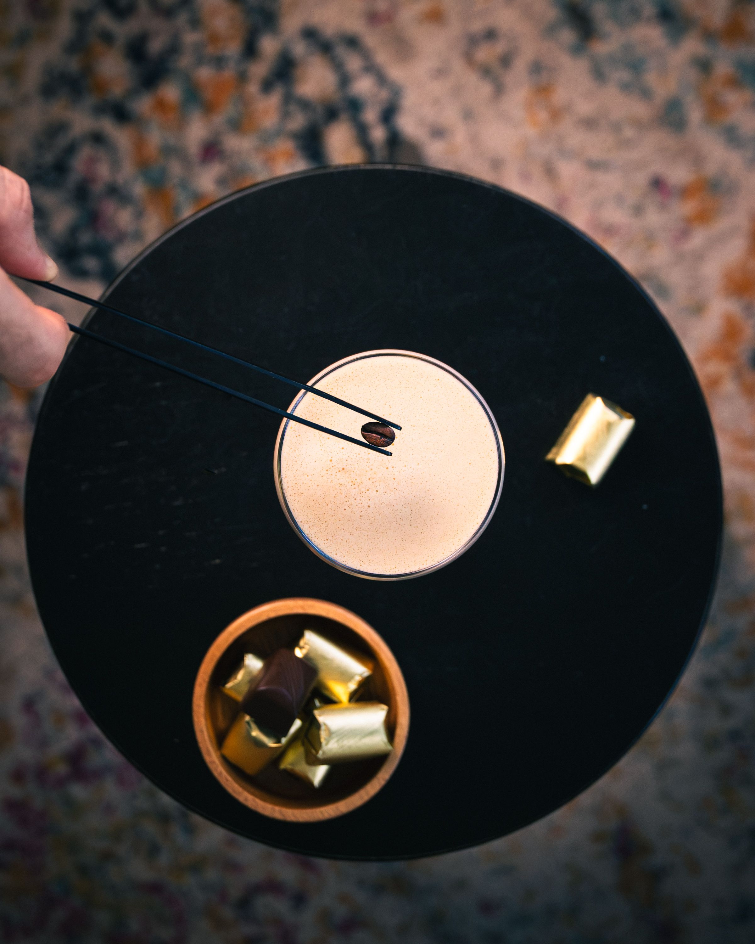 Top-down espresso martini on a black marble tray with coffee bean and gold-wrapped chocolates