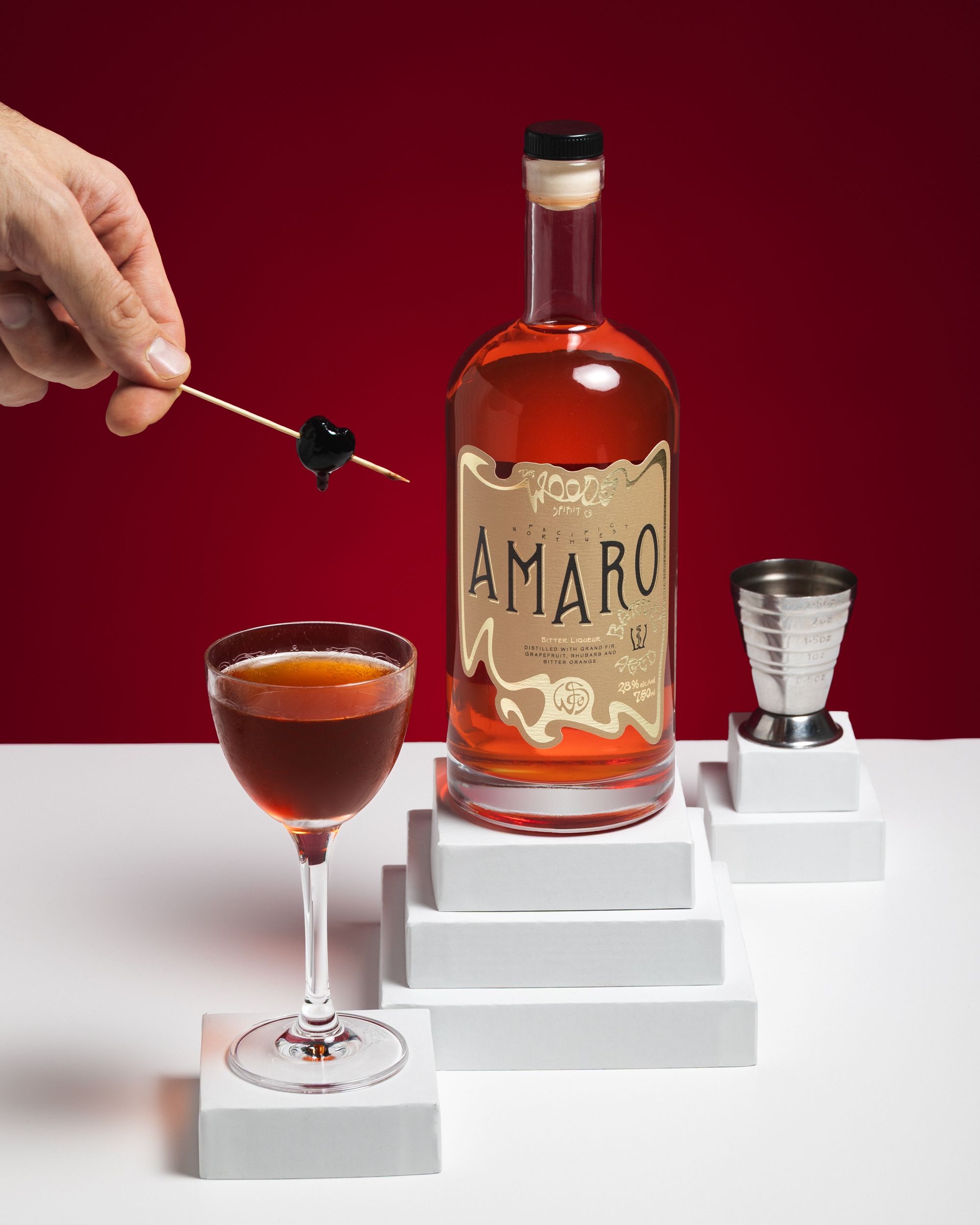 Hand placing cherry into a Wood Spirit Co Barrel Aged Amaro cocktail in coupe.