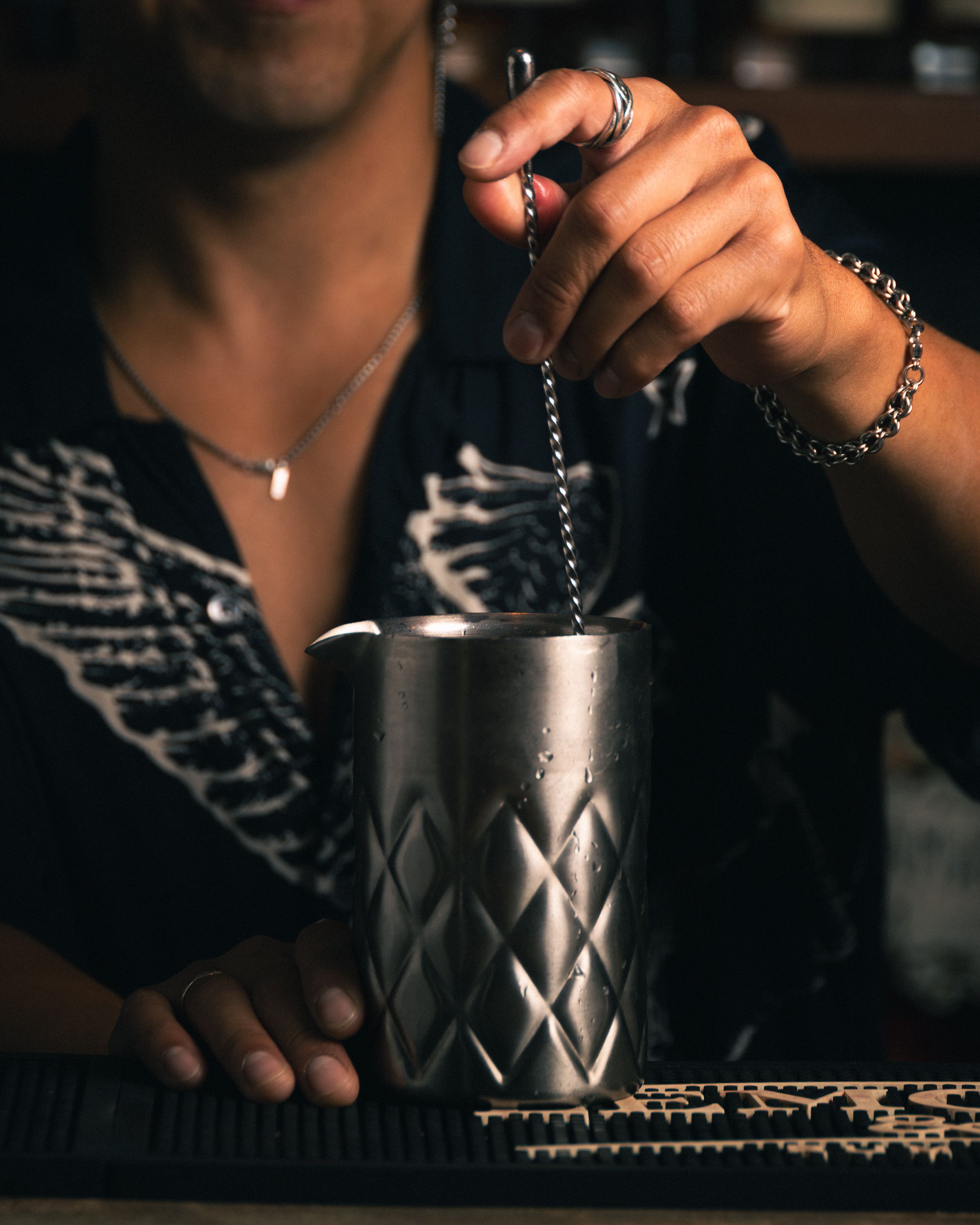 Bartender stirring a cocktail in a steel mixing tin at a bar