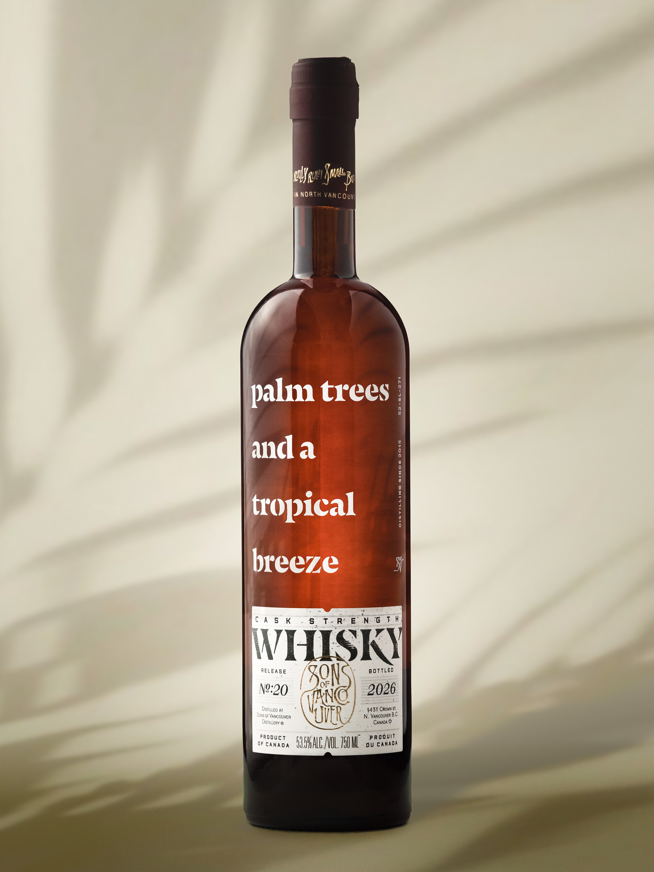 Sons of Vancouver Palm Trees and a Tropical Breeze Release #20 in its dark brown bottle against a warm tan backdrop with soft palm shadows