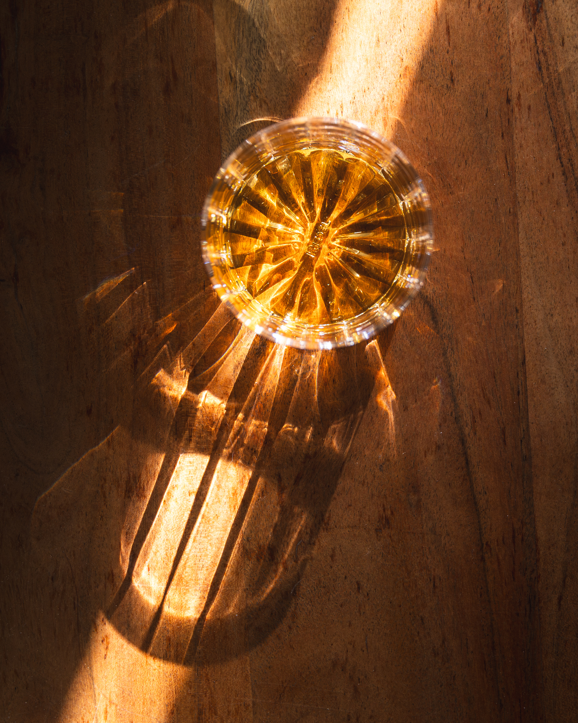 Top-down crystal whisky glass casting golden light on a warm wood surface