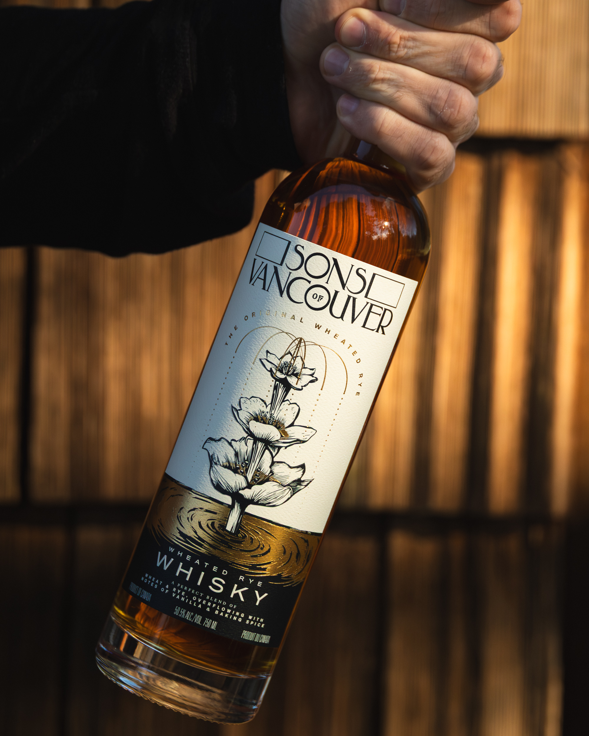 Hand gripping a Sons of Vancouver Wheated Rye bottle against warm wood