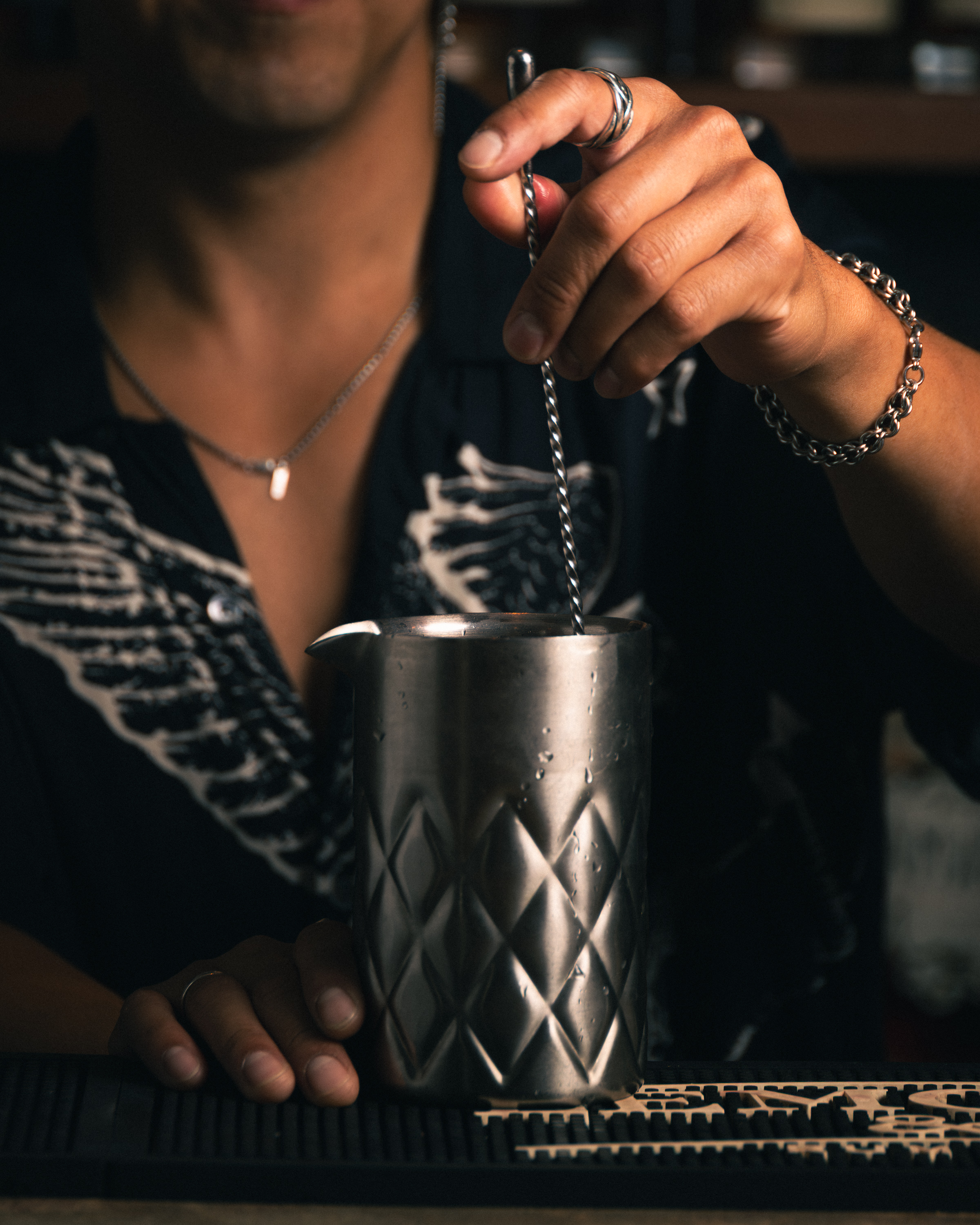 Bartender stirring a cocktail in a steel mixing tin at a bar