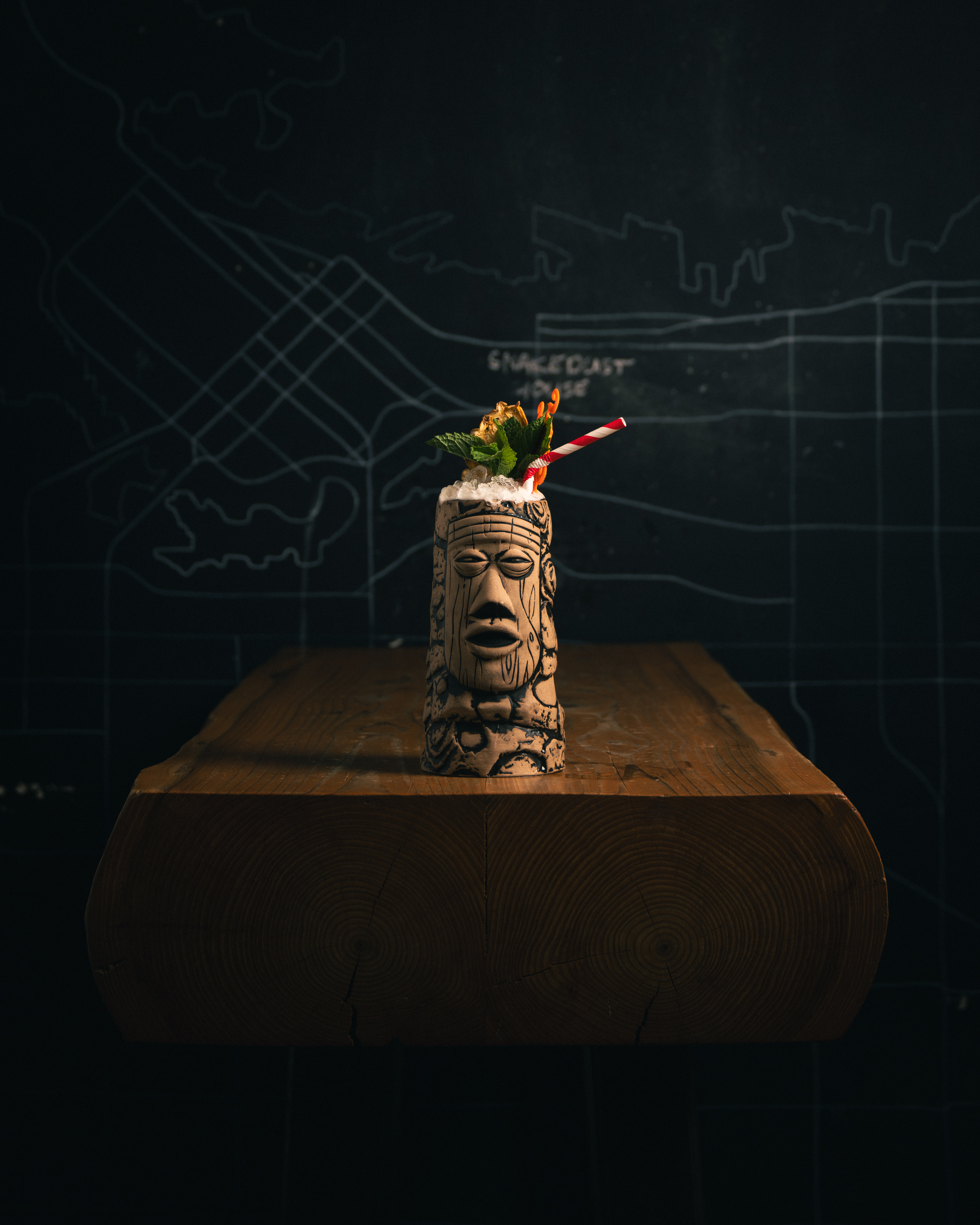 Tiki mug cocktail on an end-grain wood block against a dark chalkboard map background