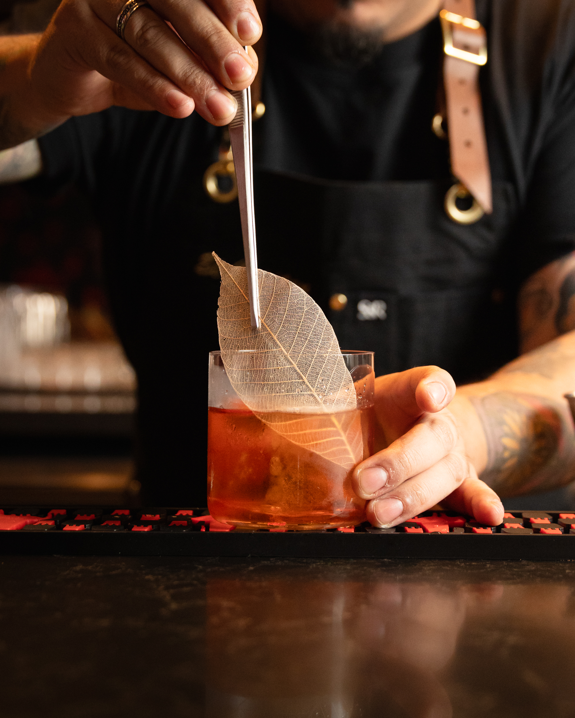 Bartender placing a skeletal leaf garnish on an amber cocktail at Terminal City Club
