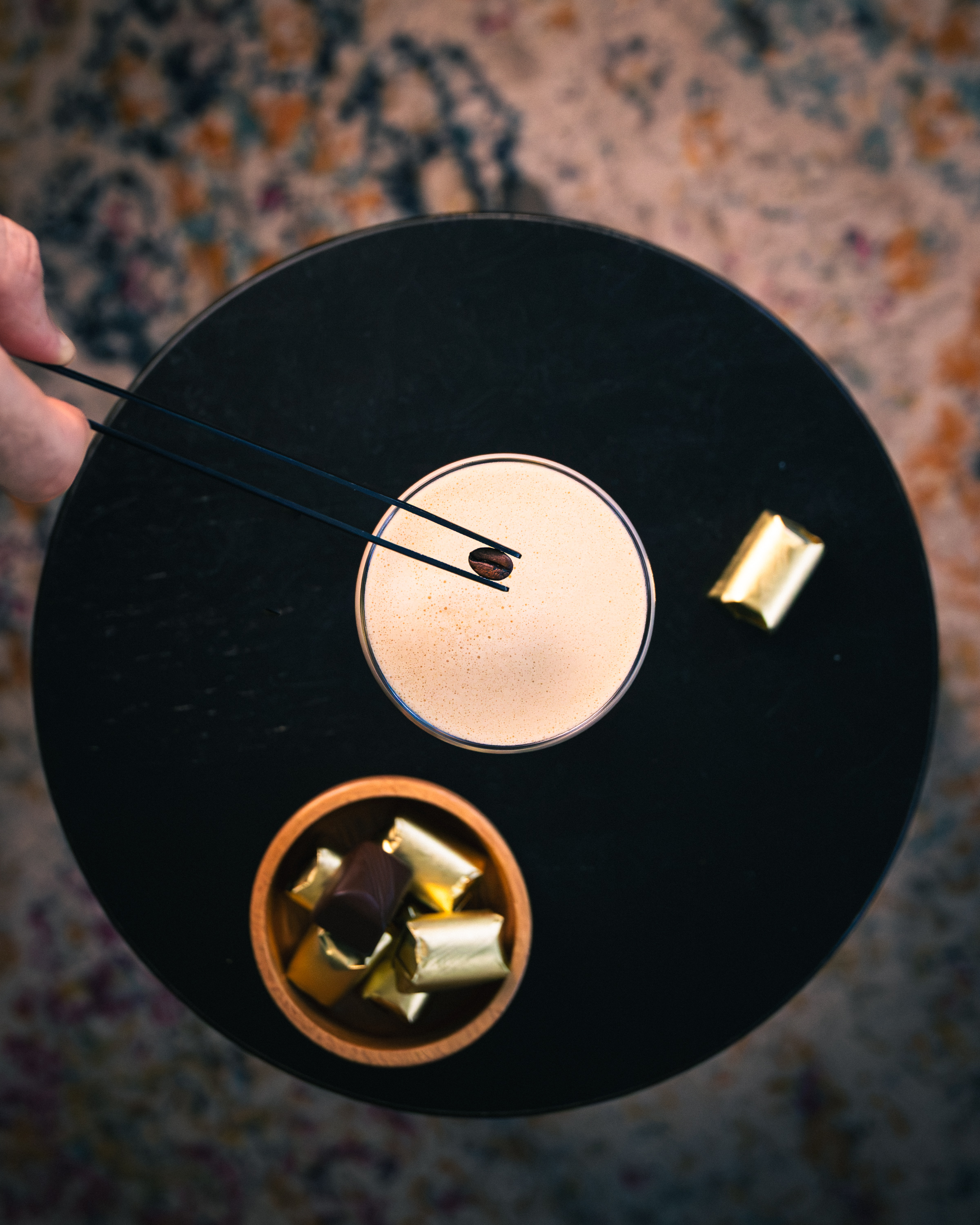 Top-down espresso martini on a black marble tray with coffee bean and gold-wrapped chocolates