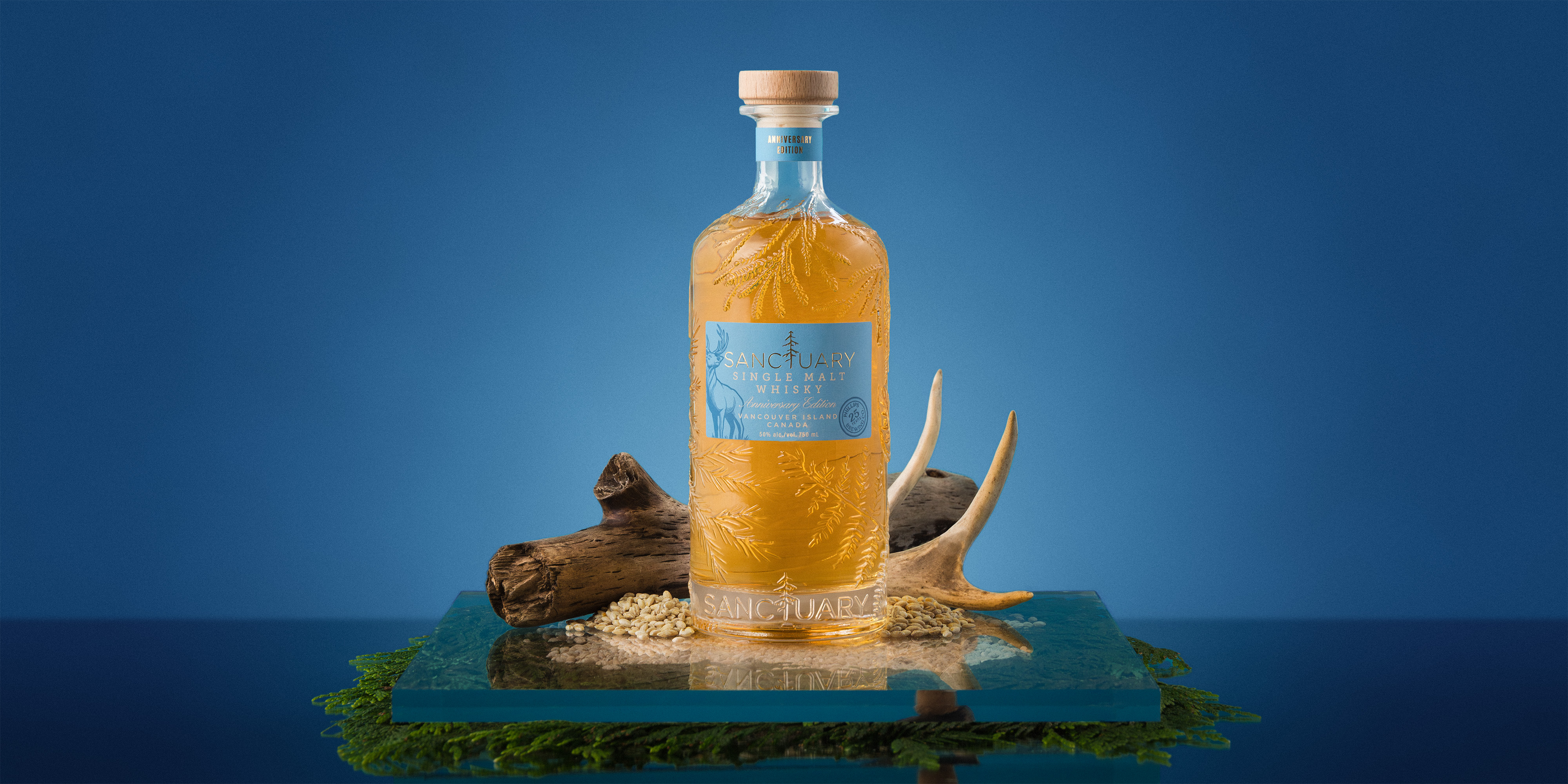 Sanctuary Anniversary Edition bottle with driftwood and antler on a blue ground, wide format