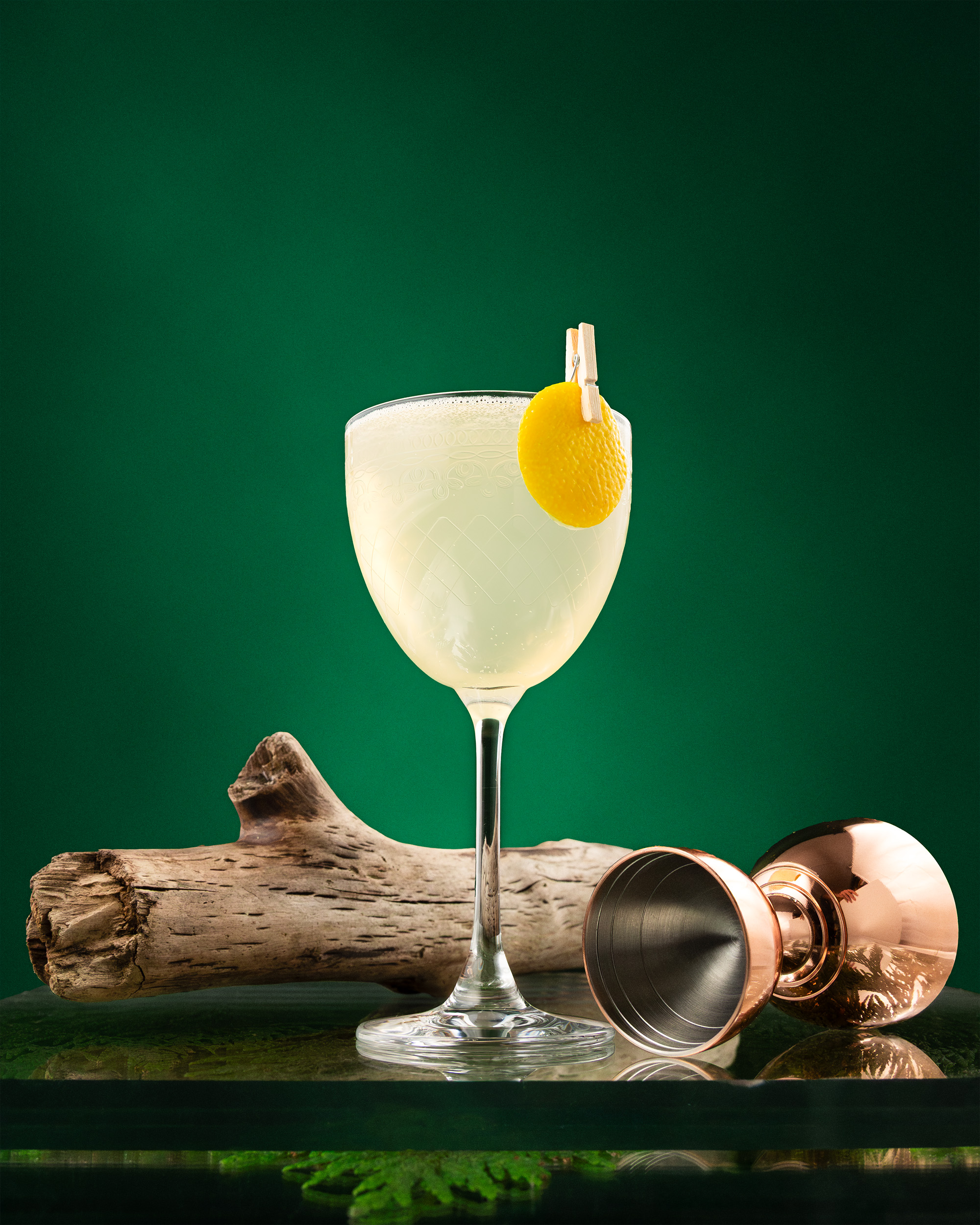 Pale Sanctuary cocktail in coupe with lemon disc and copper jigger on a green ground