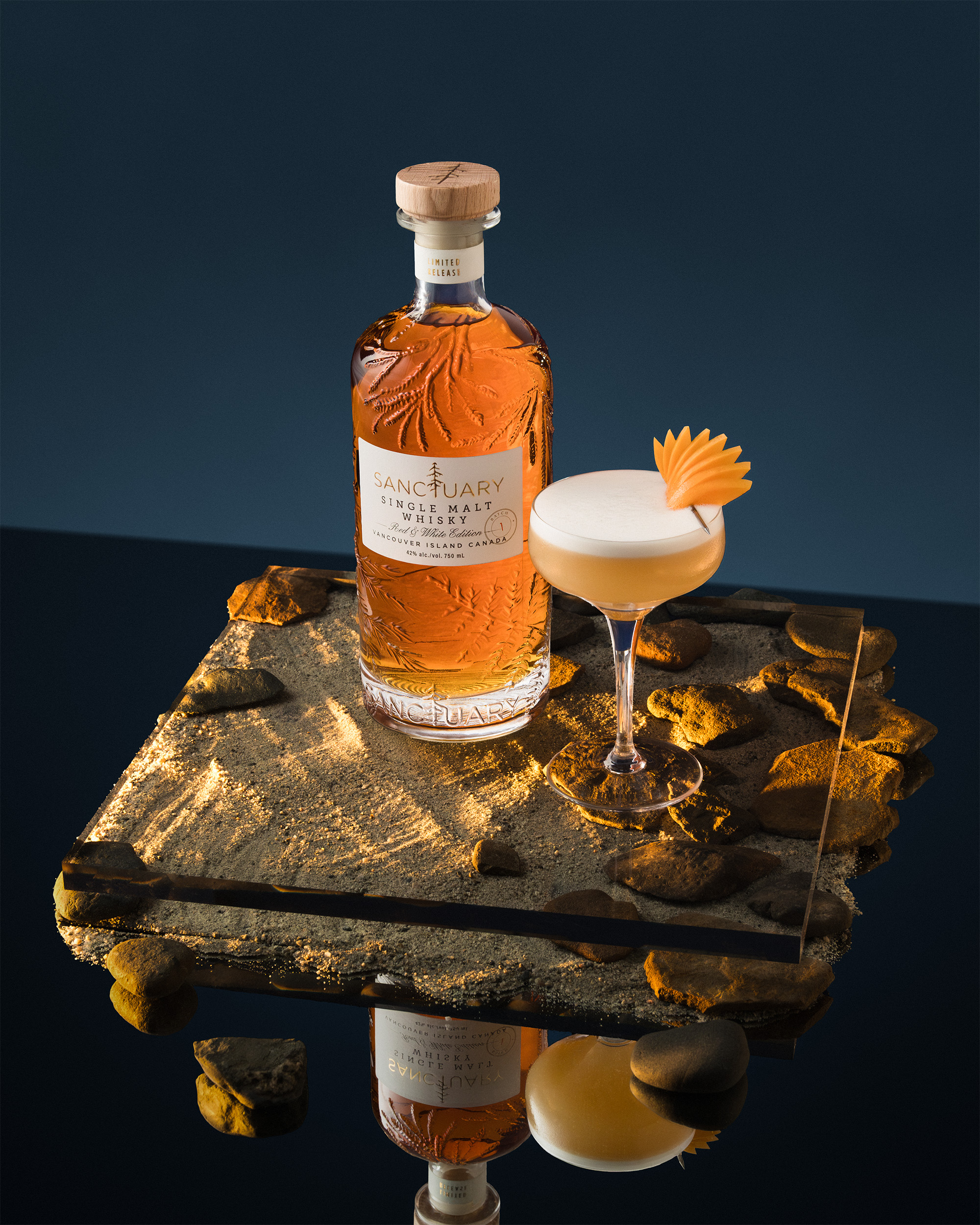 Sanctuary Red and White Edition bottle with foamy white cocktail on a rocky coastal surface