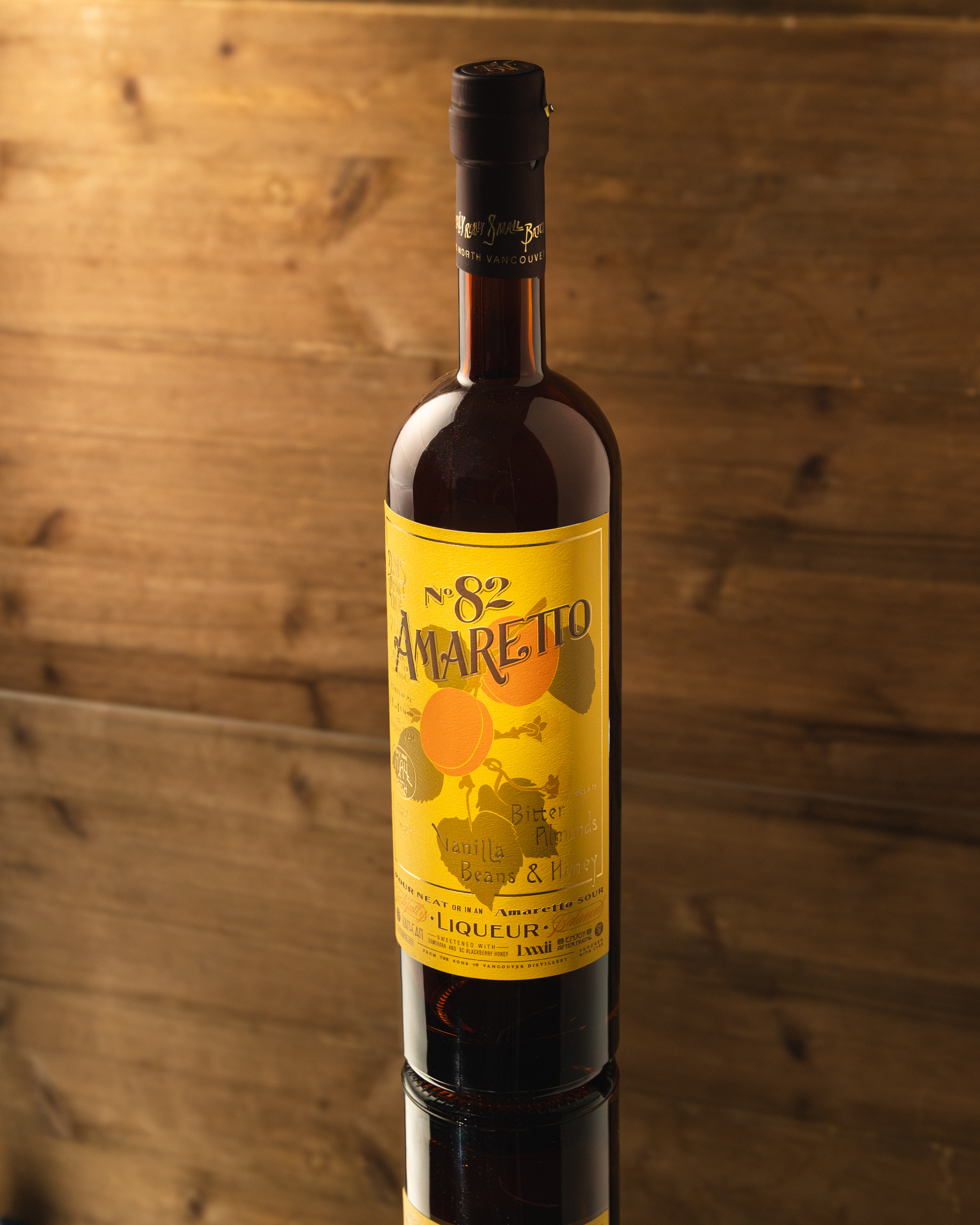Sons of Vancouver No. 82 Amaretto bottle with yellow label on warm wood