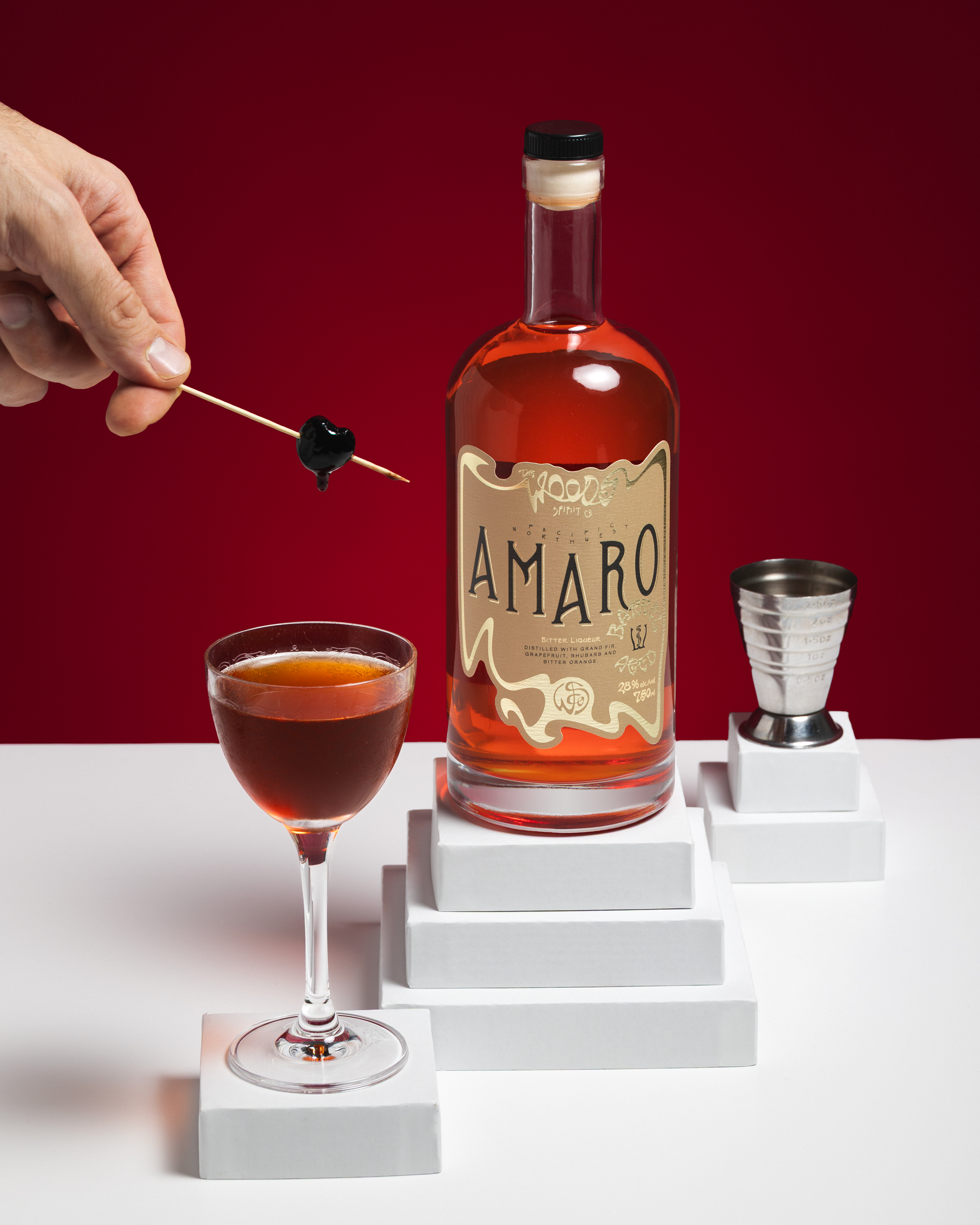 Hand placing cherry into a Wood Spirit Co Barrel Aged Amaro cocktail in coupe.